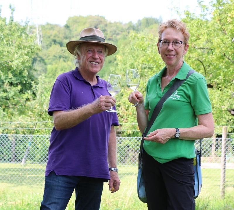 Ein Mann und eine Frau stehen auf eine Wiese und halten jeder ein Glas Weißwein in der Hand.