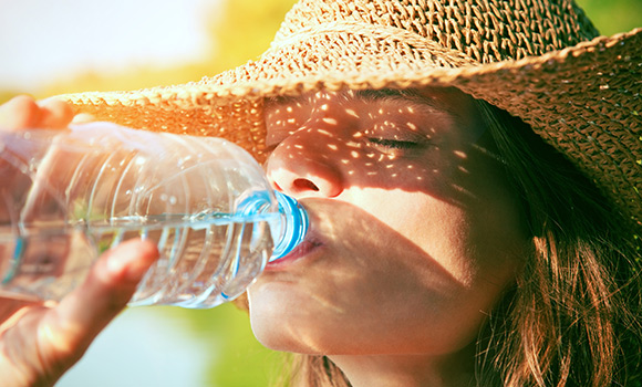 Frau mit Sonnenhut trinkt Wasser aus einer Flasche.