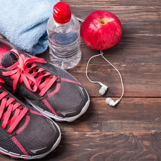 Fußboden mit Turnschuhen, Apfel, Wasserflasche, Handtuch und Kopfhörern