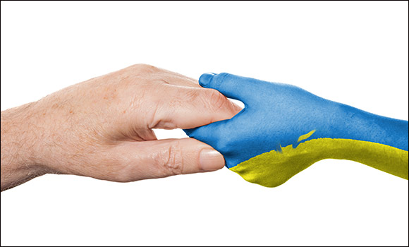 Das Symbolbild zeigt eine Hand, die eine andere Hand - gefärbt in den Nationalfarben blau und gelb der Ukraine - hält.