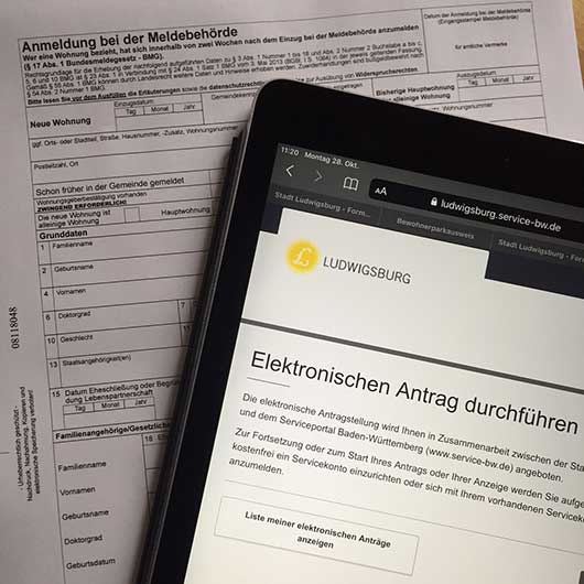 ausgedruckte Papierformulare und ein elektronischer Antrag auf einem Tablet