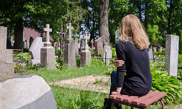 Eine Frau sitzt auf einer Bank auf einem Friedhof.