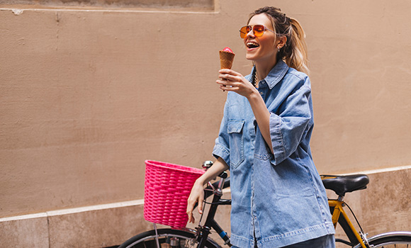 Frau schiebt ihr Fahrrad und isst ein Eis.