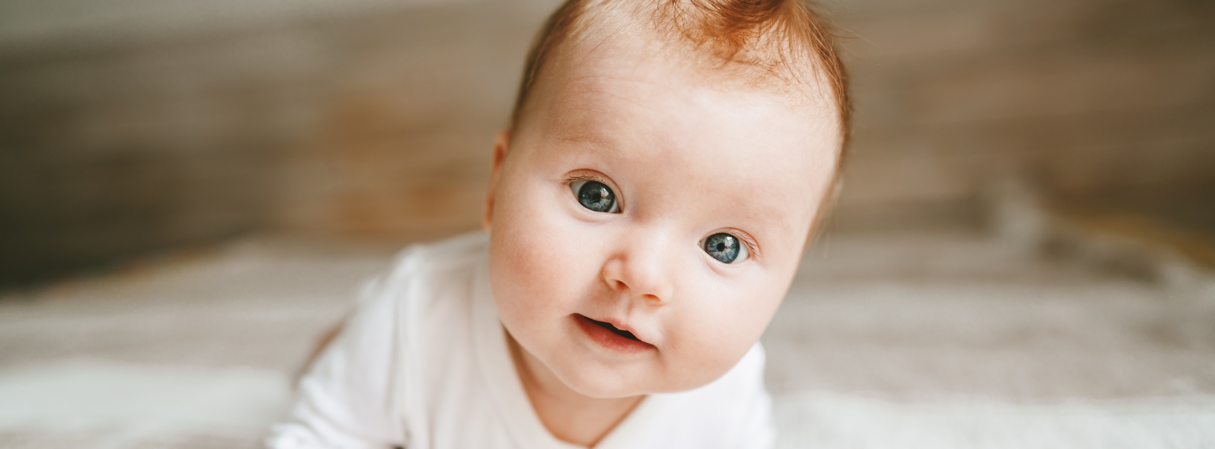 Baby auf einem weichen Untergrund, stützt sich mit einem Arm hoch und schaut nach vorn